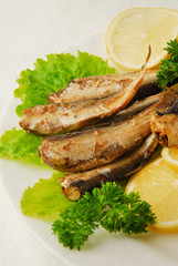 Pan-fried spiced sprats with lemon, salad on a plate