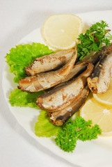 Pan-fried spiced sprats with lemon, salad on a plate