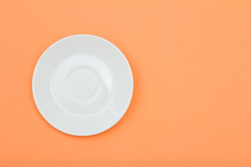 White porcelain saucer on peach color background.