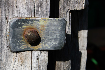 vintage metallic element with a rusty bolt on the background of the gray wooden door in an old abandoned barn