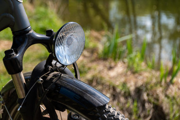 Close-up of the front of the bike with a headlamp with a blurred background of grass and pond