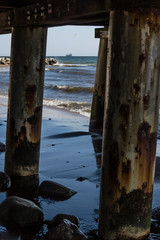 Cargo ship on the horizon seen from underneath wooden pier. Ship is in focus, pillars in foreground out of focus