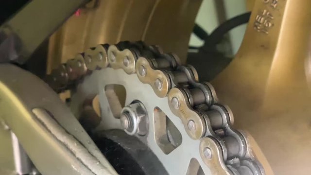Oiling a motorcycle chain in a workshop. Woman is lubricating moto chain with lube. Closeup of spraying motorbike chain with oil lubricant.