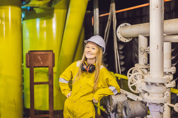 Young woman in a yellow work uniform, glasses and helmet in industrial environment,oil Platform or liquefied gas plant