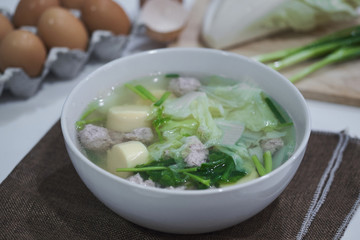Clear soup with vegetables egg tofu and minced pork on table