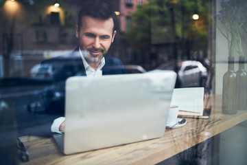 Smiling businessman working with laptop in modern cafe