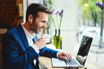 Businessman having videocall on laptop while drinking coffee in cafe