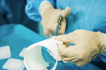 A nurse with latex gloves cuts strips of bandage in preparation to care for an injured person.