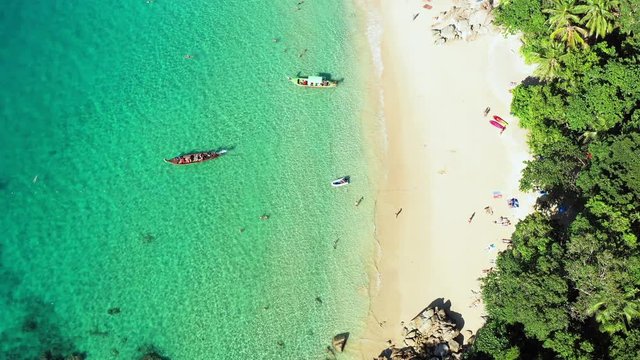 View from above, aerial view of a beautiful tropical beach with white sand and turquoise clear water, longtail boats and people sunbathing, Banana beach, Phuket, Thailand.