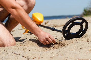 A man with a metal detector on the beach picks up a find from the sand