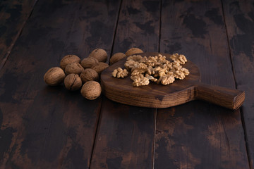 Cracked and whole walnuts lying on cutting board and wooden table, side view. Healthy nuts and seeds composition.
