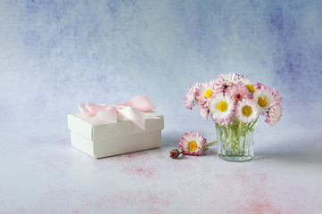 White gift with vase of pink daisies on ligth background. Greeting card. Minimalism, soft focus, copy space.