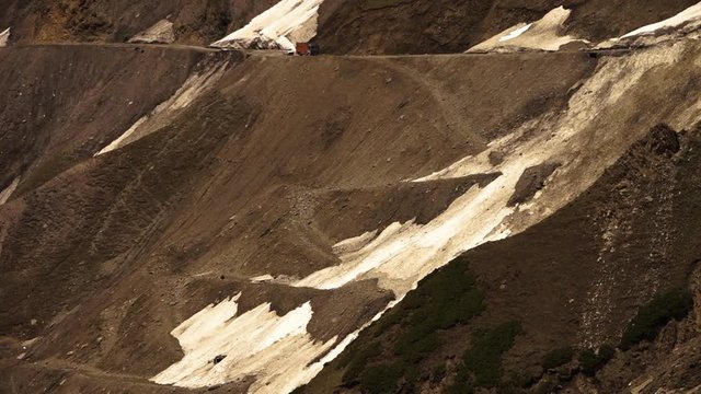 Close up, low angle view of a dangerous mountain road, ZojiLa pass. Its drainage channel is filled with glaciers. Small bumps control their downward flow. Vehicles slowly moving uphill, Ladakh