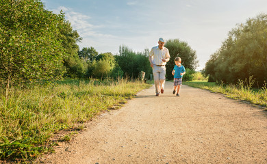 Front view of senior man with hat and happy child running on a nature path. Two different generations concept.