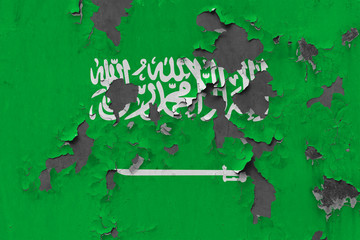 Close up grungy, damaged and weathered Saudi Arabia flag on wall peeling off paint to see inside surface.