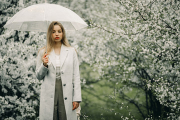 A woman relaxes with umbrella in her hands among blossoming trees.