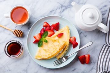 Crepes, thin pancakes with cream cheese, ricotta and fresh strawberries. Marble background. Top view.
