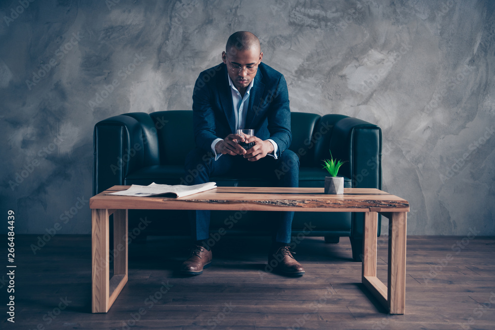 Wall mural Portrait of his he nice stylish trendy classy imposing elegant attractive guy top manager company director sitting on couch drinking beverage at workplace station gray concrete wall