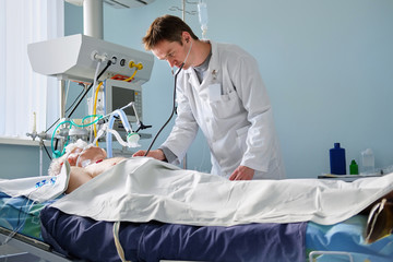 Intensive care caucasian doctor examines intubated critical stance patient writing notes to case...
