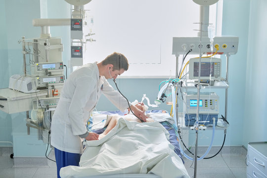 Intensive Care Caucasian Doctor Examines Intubated Critical Stance Patient In Intensive Care Department