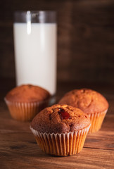 Fresh juicy muffins and a glass of milk on rustic wooden background