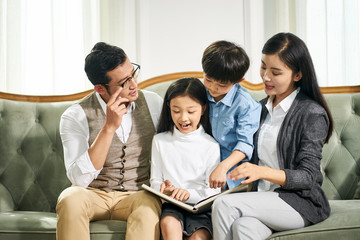 asian parents and two children reading book together