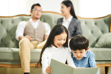 two asian children reading book together at home