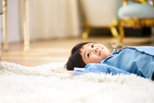 little asian boy lying on back on carpet