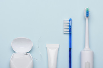 Electric sonic toothbrush with dental floss toothpaste and classic tooth brush on blue background flat lay.