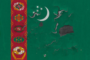 Close up grungy, damaged and weathered Turkmenistan flag on wall peeling off paint to see inside surface.