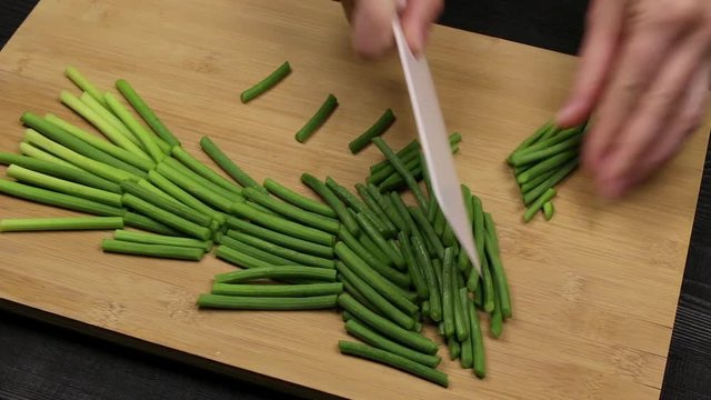 Slicing green sprouts of garlic as part of the process of making an aromatic additive to the dish according to a homemade recipe.