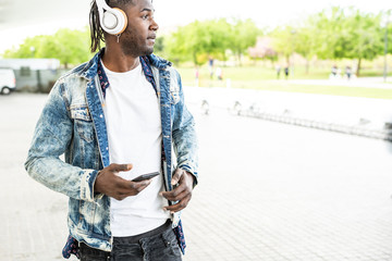African American Guy looking at the mobile phone and with music headphones. Technology and young...
