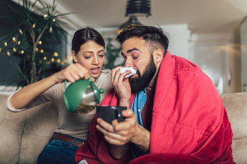 Woman taking care of her sick boyfriend lying on the sofa