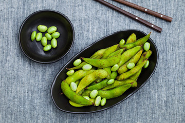 Fresh edamame green beans in black bowl. Grey background. Top view. Copy space.