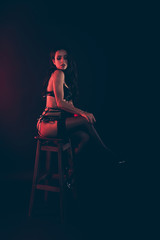 Vertical of nice lovely magnificent delicate attractive fit thin wavy-haired lady wearing swordbelt sitting on chair bar stool isolated over red light black background
