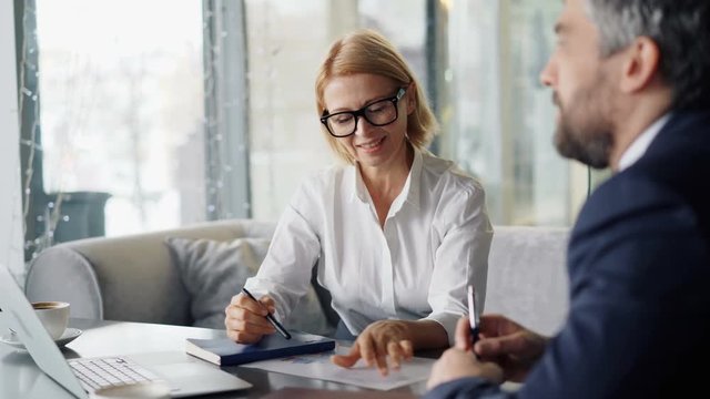 Senior woman successful entrepreneur is negotiating contract with business partner bearded middle aged man in cafe. Negotiations, restaurant and people concept.