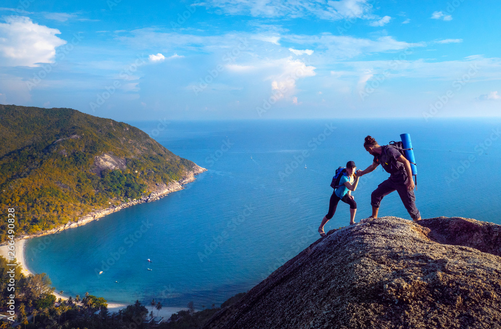 Wall mural man and woman hiking on the top of cliff in summer mountains at morning time and enjoying view of na