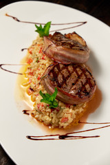Meat medallions in bacon with rice. Dark wooden background. Restaurant menu