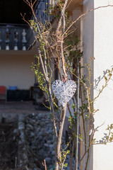 Nahaufnahme eines weißen, geflochtenen Herz, aufgehängt an einem Rosenstrauch