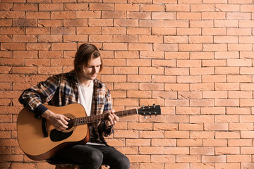 Handsome young man playing guitar against brick wall