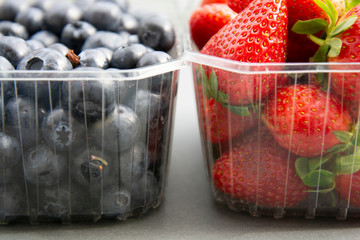 Berries in a plastic container. Fresh strawberry and blueberry in plastic box, isoalted on grey background. Natural sun light.