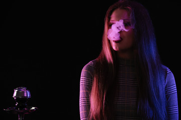 Young woman smoking hookah on dark background