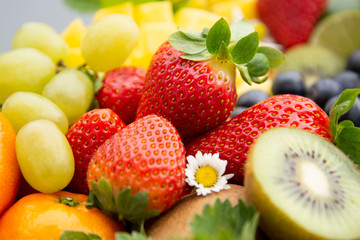 Various fresh fruits - mango, grapes, tangerine, lime, strawberry, kiwi, mint, on wooden tray and a gray background.