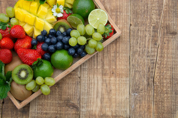 Various fresh fruits - mango, grapes, tangerine, lime, strawberry, kiwi, mint, on wooden tray with copy space.