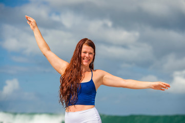  young happy and attractive red hair woman having fun standing on rock at the sea enjoying beach holidays at tropical destination isolated on blue sky