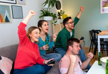 Group of friends sitting on sofa in living room and playing video games at home.