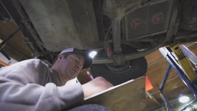 A mechanic completes data on a sheet about the maintenance of a vehicle