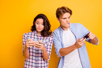 Close up photo of pair teenagers he him his she her lady boy with telephones in arms amazed with playing video games stuff wearing casual plaid shirts outfit isolated on yellow orange background