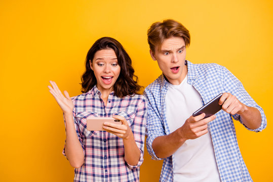 Close up photo of pair teenagers he him his she her lady boy with telephones in arms great win and big lose wearing casual plaid shirts outfit isolated on yellow orange background