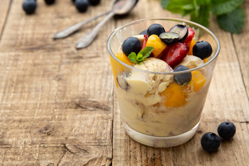 Vanilla ice cream with fruits - blueberries, strawberries, mango and mint, summer refreshing dessert. Wooden background. Glass with vanilla icecream.